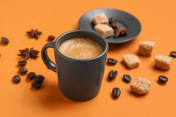 Cup of hot espresso, sugar and coffee beans on orange background
