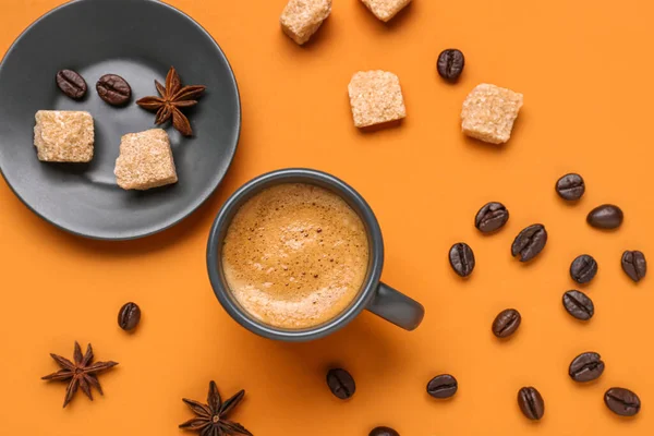 Cup of hot espresso, sugar and coffee beans on orange background