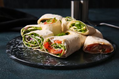 Lezzetli lavaş ruloları ve siyah arka planda sebzeler.