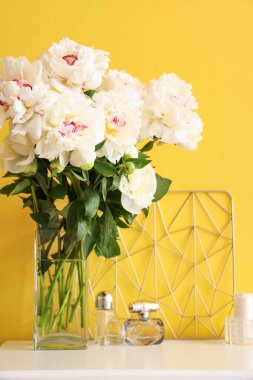 Sarı duvarın yanındaki masada parfümlü beyaz şakayık vazosu.