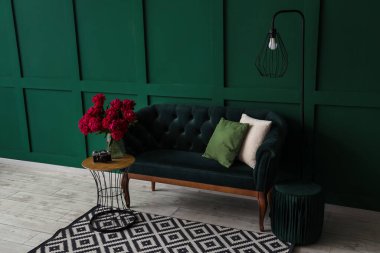 Sehpalı kırmızı şakayık vazosu, kanepe ve yer lambası yeşil duvarın yanında.