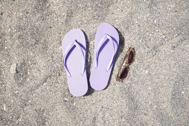 Kumsalda güneş gözlüklü leylak rengi terlikler.