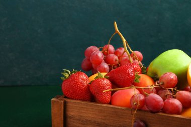 Tahta kutu ve yeşil masada farklı taze meyveler.