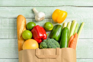 Yeşil ahşap arka planda farklı ürünler içeren kağıt torba.