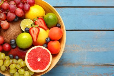 Mavi ahşap arka planda farklı taze meyvelerle dolu bir kase.