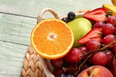 Yeşil ahşap arka planda farklı taze meyveler içeren sepet, yakın plan.