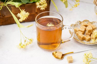 Beyaz arka planda şekerli bir bardak ıhlamur çayı ve tabak.