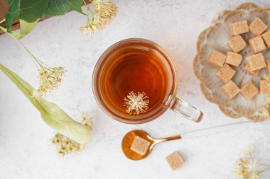 Beyaz arka planda şekerli bir bardak ıhlamur çayı ve tabak.