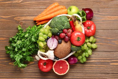 Tahta arka planda farklı taze meyve ve sebzelerle dolu sepet.