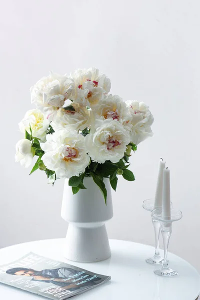 壁の近くのコーヒーテーブルの上にキャンドルや雑誌と白い牡丹の花瓶 — ストック写真