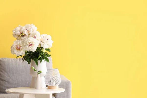 黄色の壁の近くにコーヒーテーブルとソファ付きの白い牡丹の花瓶 — ストック写真