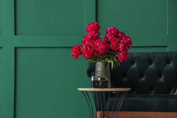 Vase of red peonies with camera, coffee table and couch near green wall