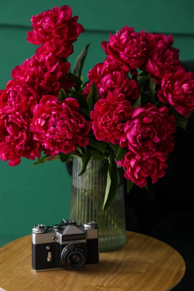 Vase of red peonies with camera on coffee table near green wall