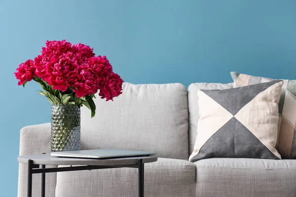 コーヒーテーブルと青の壁の近くのソファ付きの赤い牡丹の花瓶 — ストック写真