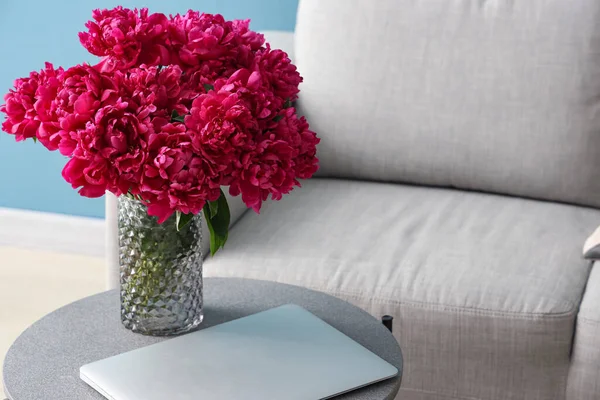 Vase of red peonies with laptop on coffee table near couch