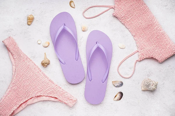 stock image Lilac flip-flops with swimsuit and shells on white grunge background