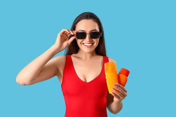 Junge Frau Mit Flaschen Sonnencreme Auf Blauem Hintergrund — Stockfoto