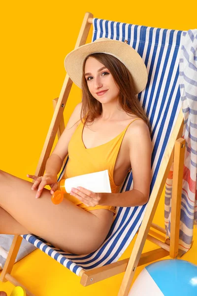 Mladá Žena Použití Krém Opalování Palubě Židle Žlutém Pozadí — Stock fotografie