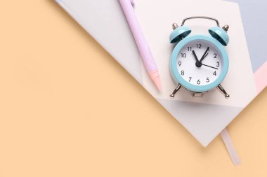 Renk arkaplanı üzerine not defteri, kalem ve alarm saati