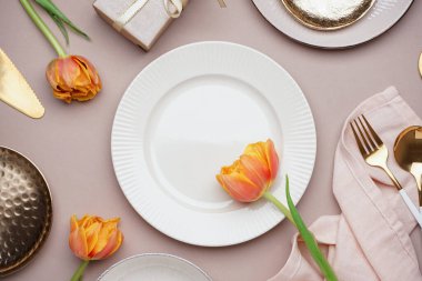 Temiz tabaklar, lale çiçekleri ve bej arka planda çatal bıçak takımı.