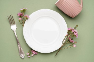 Yeşil zemin üzerinde temiz tabak, çatal, bardak ve çiçek dekoru olan kompozisyon