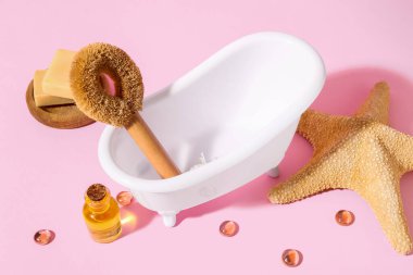 Küçük küvet, banyo malzemeleri ve pembe arka planda denizyıldızı.