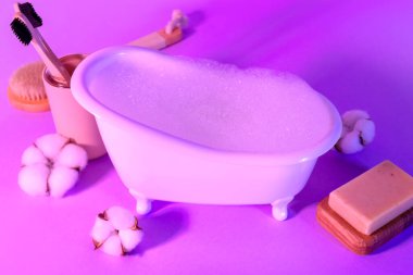 Arka planda köpük, diş fırçası, sabun ve pamuk çiçekli küçük küvet