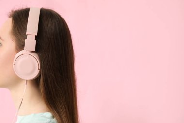 Young woman in headphones listening to music on pink background