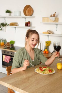 Genç bir kadın bir bardak şarapla mutfakta lezzetli makarna yiyor.