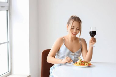 Lezzetli bir makarna ve bir bardak şarapla restoranda oturan genç bir kadın.