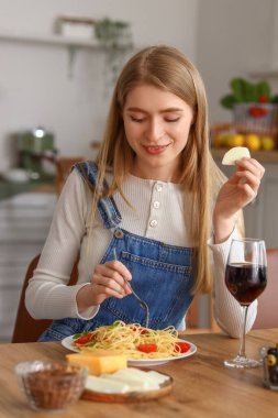 Genç bir kadın bir bardak şarapla mutfakta lezzetli makarna yiyor.