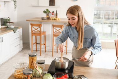 Genç bir kadın mutfakta makarna pişiriyor.