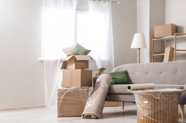 Sofa with rolled carpet and cardboard boxes in living room on moving day clipart