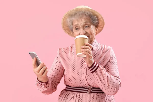 Mulher Sênior Com Telefone Celular Bebendo Café Fundo Rosa — Fotografia de Stock