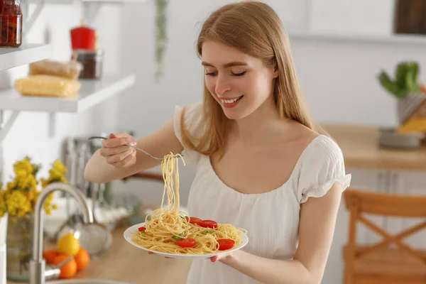 年轻女人在厨房里吃着美味的意大利面 — 图库照片