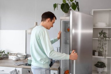 Yakışıklı adam mutfakta buzdolabı açıyor.