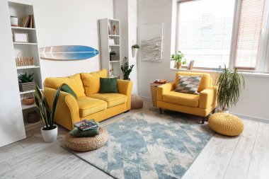 Sörf tahtası, sarı kanepesi ve koltuğu olan bir oturma odası.