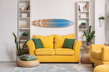 Sörf tahtası, sarı kanepesi ve koltuğu olan bir oturma odası.