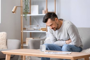 Evde karın ağrısı çeken, bir bardak suda çözünür tabletli genç adam.