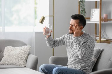 Evinde baş ağrısı çeken çözünmüş tabletli genç bir adam.