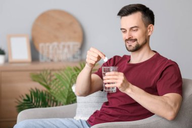 Genç adam evdeki su bardağına çözünebilir tablet koyuyor.