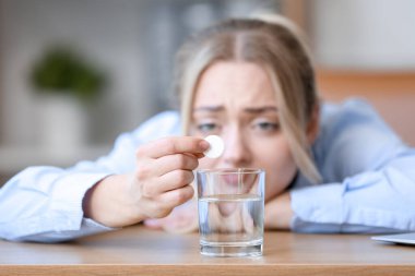 Genç iş kadını ofisteki su bardağına çözünebilir tablet koyuyor.