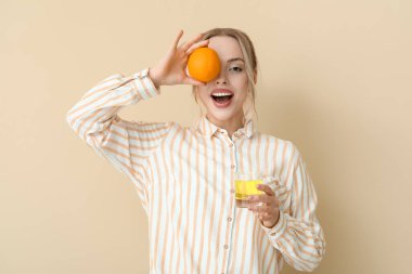 Bir bardak suda çözünmüş tableti olan genç bir kadın ve bej arka planda turuncu.