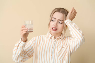 Çözülebilir tableti ve bej arka planda bir bardak suyu olan hasta genç bir kadın.