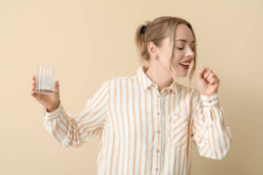 Bir bardak suda çözünmüş tabletle bej arka planda öksüren genç bir kadın.