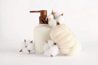 Hafif arka planda bir şişe kozmetik ürünü, banyo süngeri ve pamuk çiçekleri.