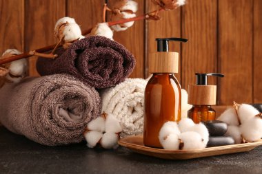 Kozmetik ürünler şişeleri, banyo malzemeleri ve pamuk çiçekleri ile karanlık masa üzerinde ahşap arka plan, yakın çekim