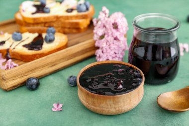 Bir kase tatlı yaban mersini reçeli ve yeşil masada leziz kızarmış ekmek.