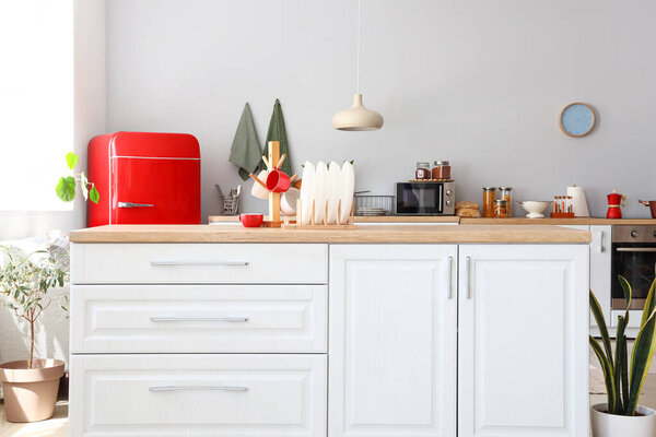 Интерьер светлой кухни с красным холодильником, прилавками и комнатными растениями