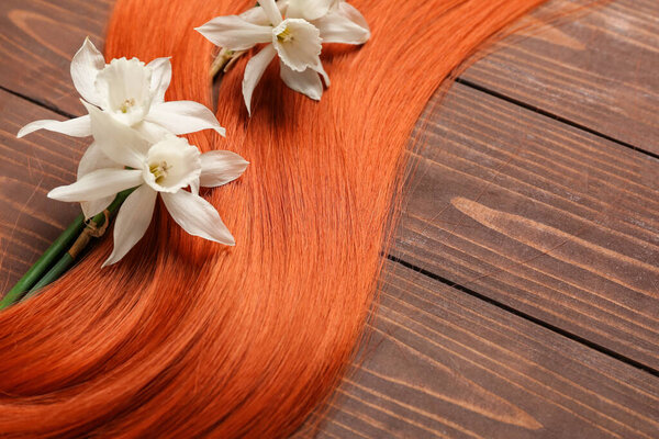 Ginger hair strand with beautiful narcissus flowers on wooden background, closeup